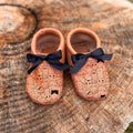Pair of baby shoes with black bows on a wooden surface