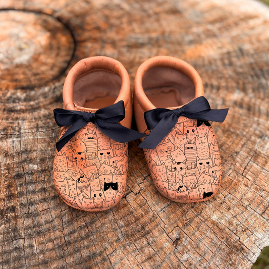 Pair of baby shoes with black bows on a wooden surface