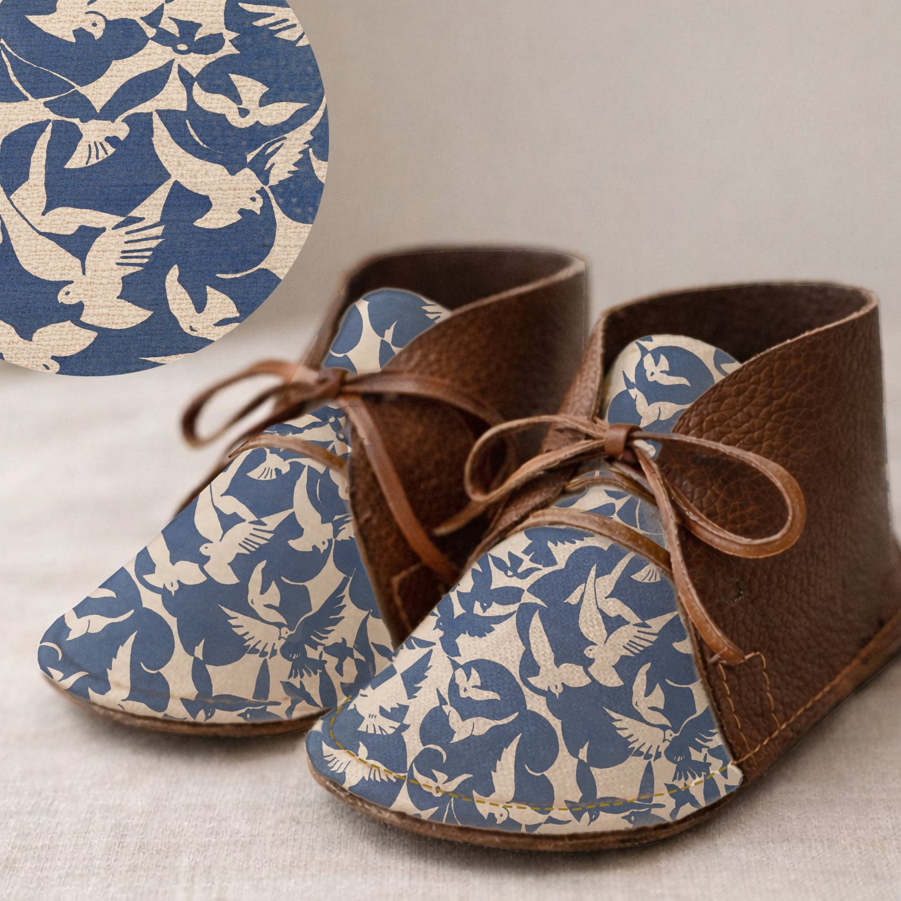Pair of brown leather baby shoes with blue and white pattern on a neutral background