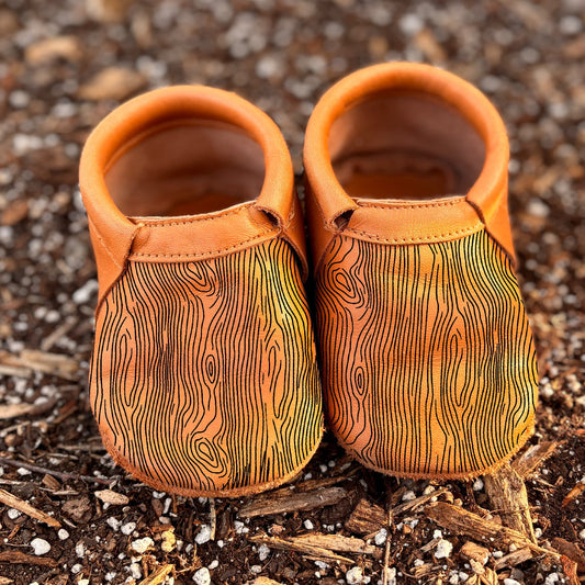 Pair of small brown leather shoes with wood grain pattern on a textured brown surface